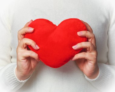 Beyaz örgü kazak kırmızı yumuşak kalp şekli tutan genç kadın. 