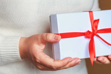 Ellerini beyaz hediye kutusunda tutan örgü beyaz kazaklı genç kadın 