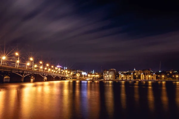 Puente Chernavsky iluminado por la noche, vista a la orilla derecha o al centro de la ciudad de Voronezh, paisaje urbano dramático con reflejo — Foto de Stock