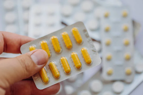 Cápsulas de medicina na mão de perto no fundo borrado de muitos comprimidos, pílulas e medicamentos — Fotografia de Stock