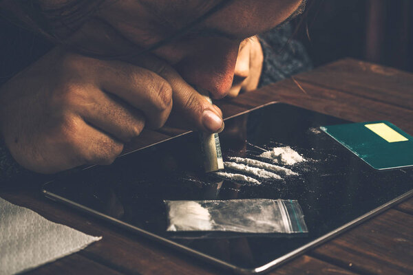 Junkie snorting cocaine powder with rolled dollar banknote. Narcotics and drug abuse concept