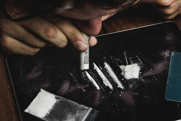Наркоман нюхает кокаиновый порошок со свернутой банкнотой. Концепция наркотиков и наркомании — стоковое фото