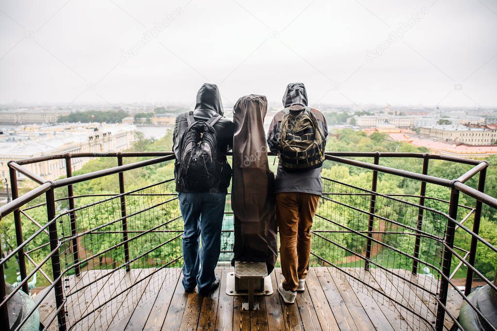 Two men tourists on the observation deck on the roof of St. Isaac's Cathedral in St. Petersburg on a cloudy day admiring the urban landscape