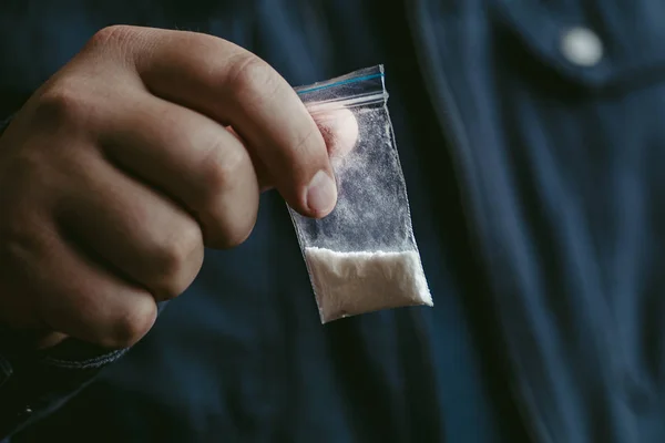 Mans mão contém pacote de plástico com pó de cocaína ou outra droga. Traficante de drogas vendendo drogado — Fotografia de Stock