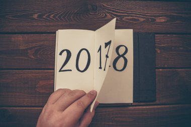 Yeni yıl 2018 önümüzdeki kavramdır. El ahşap masa üzerinde Not Defteri sayfası döndürür. 2017 dönüyor, 2018 açma