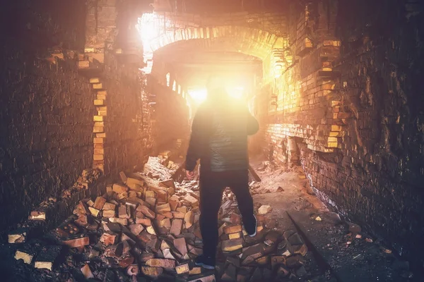 Man in abandoned underground ruined tunnel, light from end or exit from brick creepy corridor, industrial broken mine — Stock Photo, Image