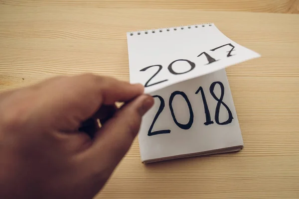 Man flips notepad sheet on table. 2017 is turning, 2018 is opening — Stock Photo, Image