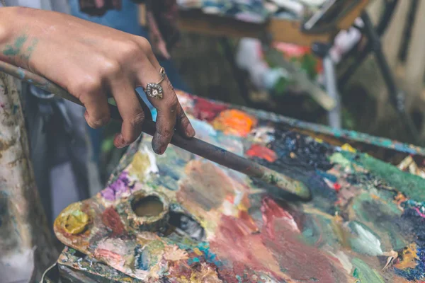 Artista pinta quadro por pincel de tinta a óleo na mão com paleta, foco seletivo, close up, tonificado — Fotografia de Stock
