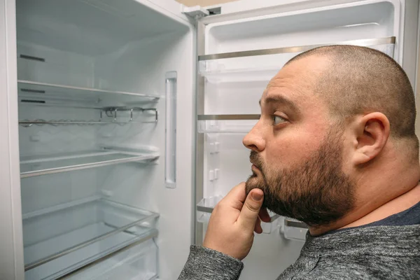 Pria gemuk lucu melihat ke dalam lemari es kosong — Stok Foto