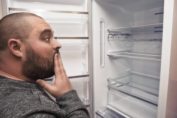 Terkejut pria gemuk lucu melihat ke dalam lemari es kosong — Stok Foto