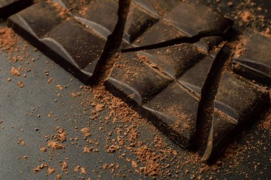 Kırık çikolata parçaları ve koyu arka plan üzerine kakao tozu