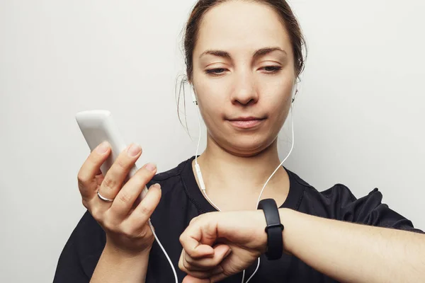 Jeune femme avec smartphone et écouteurs regardant bracelet de fitness ou traqueur d'activité intelligent avec podomètre. Style de vie sportif sain et concept de technologie moderne — Photo