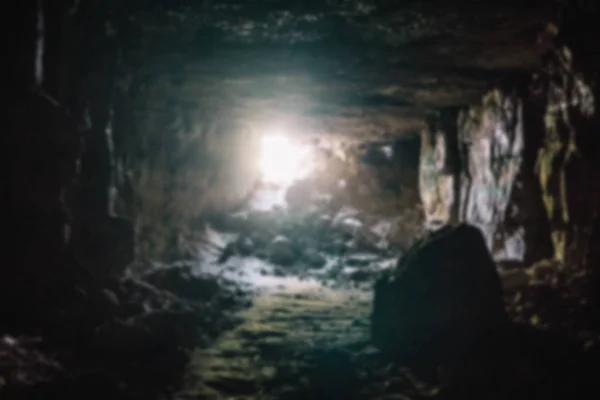 Escape from darkness concept. Blurred and defocused photo of dark underground limestone mine cave tunnel or corridor with light and exit in the end