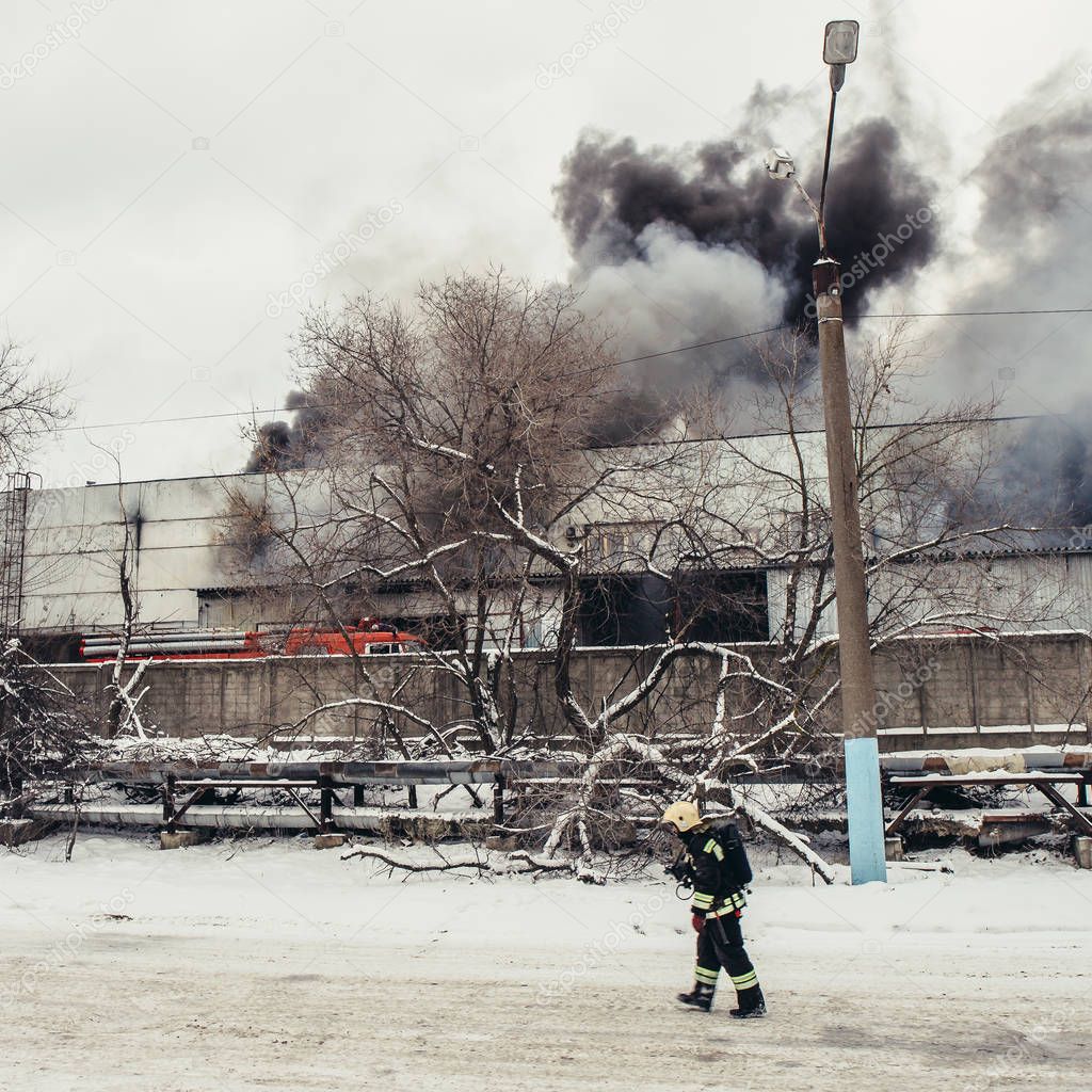 Fireman going left at burning industrial building with fire flames and black smoke background