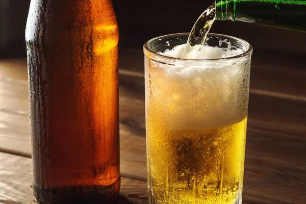 Despejando cerveja espumante em caneca de vidro com gotas perto de bebida de cerveja fria na mesa de madeira, fabricação de cerveja artesanal — Fotografia de Stock