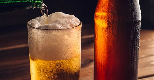 Despejando cerveja espumante em caneca de vidro com gotas perto de bebida de cerveja fria na mesa de madeira, fabricação de cerveja artesanal — Fotografia de Stock