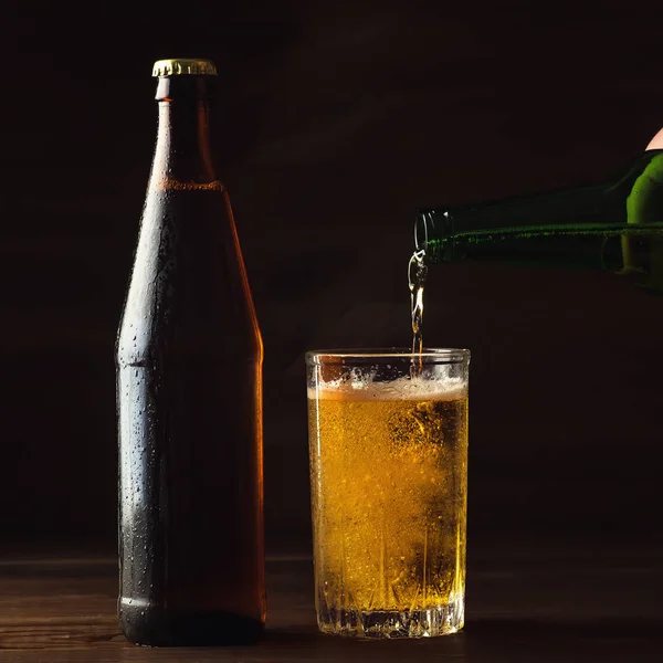 Despejando cerveja espumante em caneca de vidro com gotas perto de bebida de cerveja fria na mesa de madeira, conceito de fabricação de cerveja artesanal — Fotografia de Stock