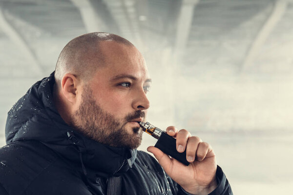 Vape man. Young guy vaping electronic cigarette or vape pen at urban background, modern lifestyle