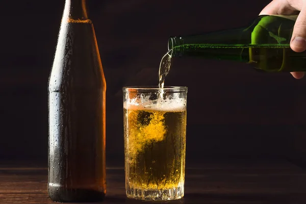 Hälla skummande öl i glas mugg med droppar nära kall öl bootle på svart bakgrund — Stockfoto