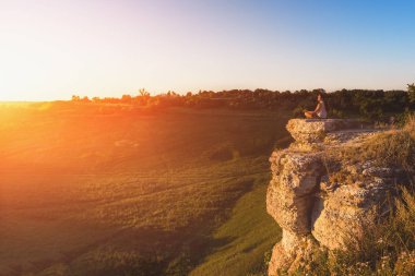 Adam dağ arka plan Rock'ta günbatımı oturan meditasyon