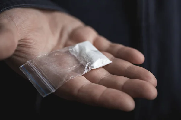 Мужская рука держит на ладони пластиковый пакет с кокаином порошок или другой наркотик. Наркоторговец предлагает попробовать наркотическую концепцию — стоковое фото