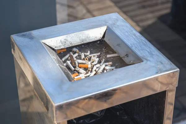 Cigarette butts or stubs in public stand-less bin near mall . Smoking is bad