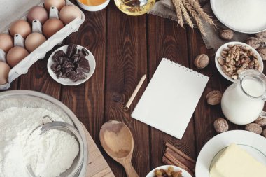 Fırın arka plan, pişirme kek malzemeler: yumurta, un, süt, tereyağı, yağ, ceviz ve kuru üzüm üzerinde ahşap masa, üstten görünüm.