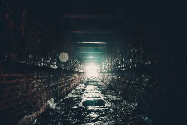 Túnel húmedo de ladrillo oscuro o corredor industrial subterráneo abandonado con luz al final — Foto de Stock