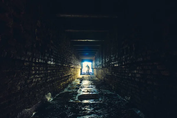 Silueta člověka s baterkou v tmavých špinavé cihlové podzemní tunel nebo kanalizace koridoru — Stock fotografie