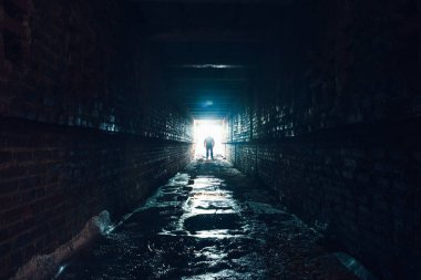 Silhouette of man standing in dark underground corridor. Light at end of tunnel concept clipart