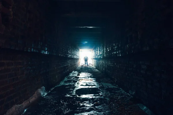 어두운 지 하 복도에 서 있는 남자의 실루엣입니다. 터널의 끝에 빛 — 스톡 사진