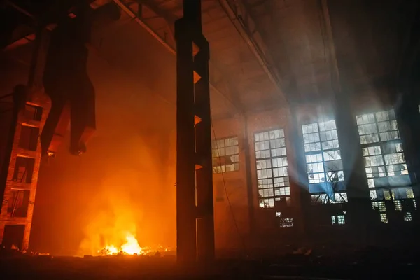 Kebakaran di aula besar pabrik atau gudang di malam hari. Api besar merah dan kuning dan cahaya biru dari jendela — Stok Foto