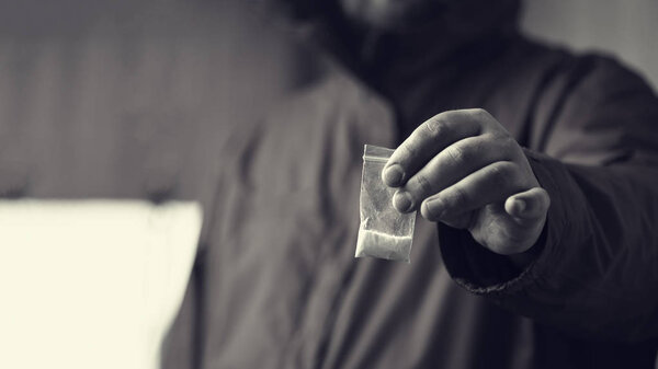 Drug dealer offers cocaine dose or another drugs in plastic bag, drug addiction on party concept, selective focus