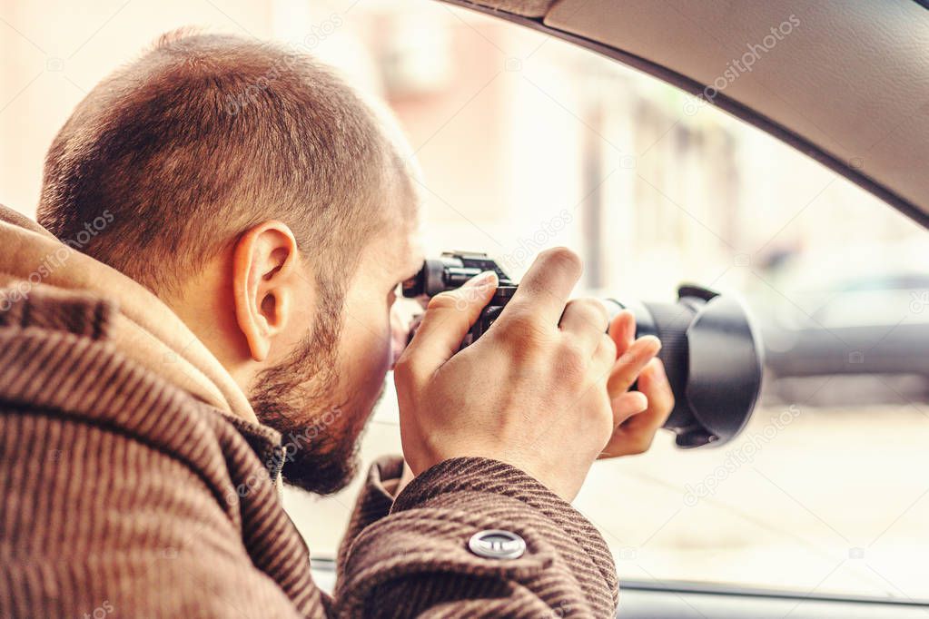 Investigator or private detective or reporter or paparazzi sitting in car and taking photo with professional camera