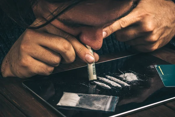 Наркоман, употребляющий наркотики, нюхающий кокаин, белый порошок с купюрой в долларах — стоковое фото