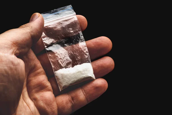 Мужская рука держит пластиковый пакет с кокаином порошок или другой наркотик на темном фоне — стоковое фото