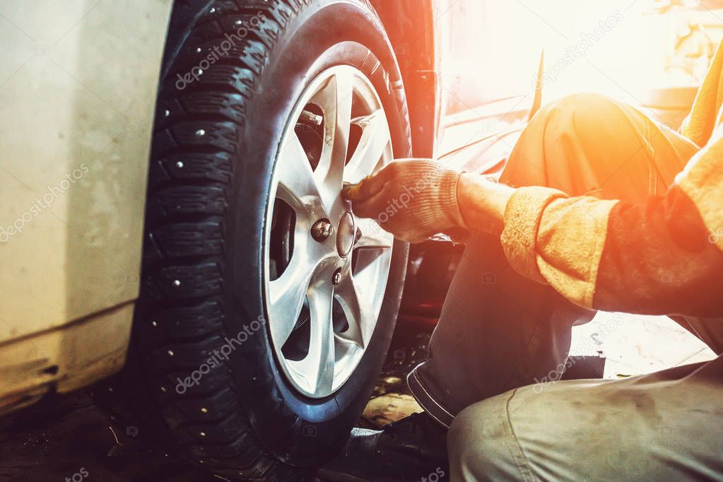 Car mechanic worker doing tire or wheel replacement in garage of repair service station