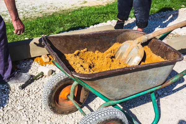 Wheelbarrow with sand and workers hands on construction site — Stock Photo, Image