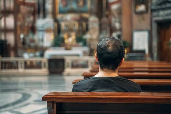 El creyente se sienta y reza en el banco dentro del viejo gran templo o iglesia, vista desde atrás — Foto de Stock