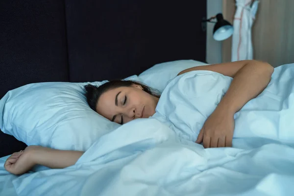 Ung vacker flicka eller kvinna sover ensam i stor säng på natten — Stockfoto