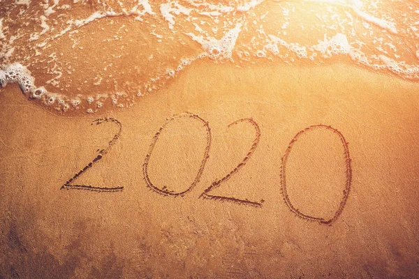 Bonne année 2020, chiffres manuscrits sur la plage de sable avec des vagues de mer à la lumière du coucher du soleil. Nouvel An, voyage et nouveau concept de départ — Photo