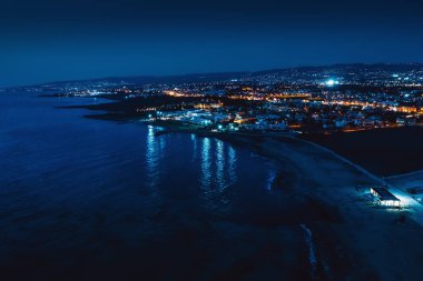 Kıbrıs Rum Kesimi, Paphos 'un hava panoramik görüntüsü, gece boyunca yukarıdan insansız hava aracı görüntüsü. Aydınlatılmış binaları ve deniz suyundaki ışıkların yansımalarıyla Akdeniz 'in güzel akşam manzarası