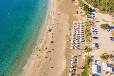 Kıbrıs, Paphos 'taki gök mavisi deniz suyuyla güzel Mercan plajı manzarası. Kum kıyısında şemsiyeler, güneşlikler, insanlar ve berrak deniz suyu.