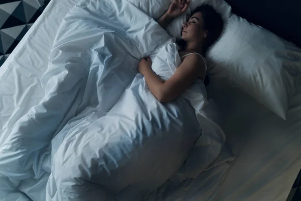 Young beautiful girl or woman sleeping alone in big bed at night, top view