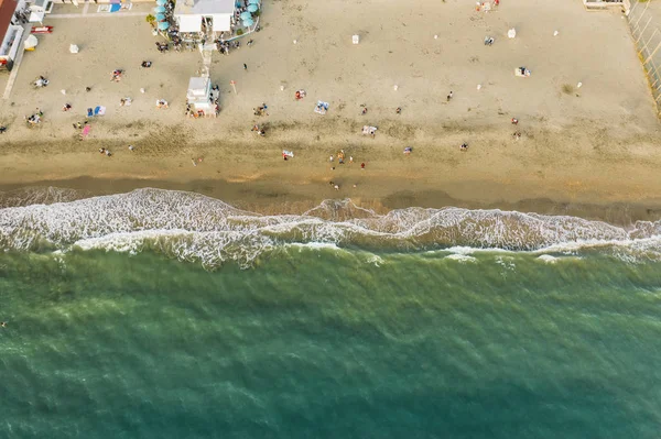 Blick von oben auf den Strand des italienischen Urlaubsortes mit Sand und schäumenden Meereswellen bei Sonnenuntergang. ostia lido bei rom, italien — Stockfoto