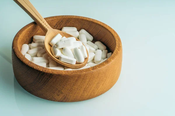 White pills or tablets in wooden spoon in wooden bowl full of medications. Organic supplements and healthy life style concept — 스톡 사진