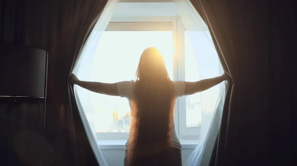 Woman opens window curtains at home for morning sunlight — Stock Photo, Image