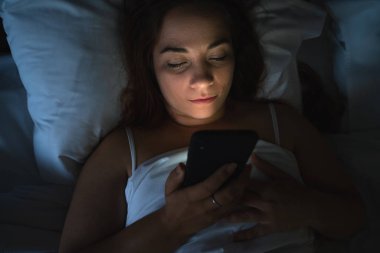 Teknoloji ve iletişim konsepti, yatakta akıllı telefonla mesajlaşan güzel bir kadın, üst görünüm.