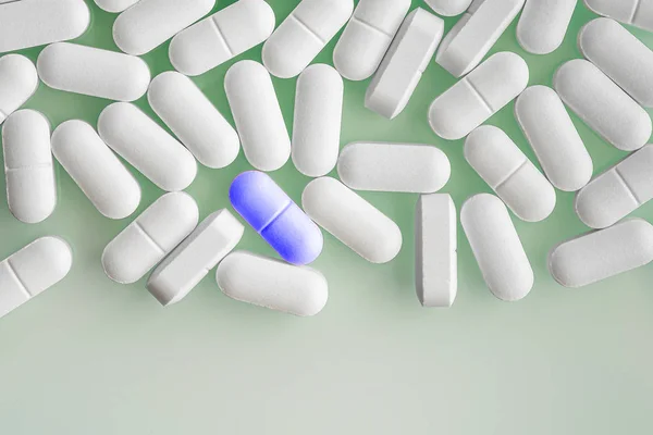 Vista dall'alto di molte capsule o pillole di farmaci bianchi e una compressa o farmaco di colore blu — Foto Stock