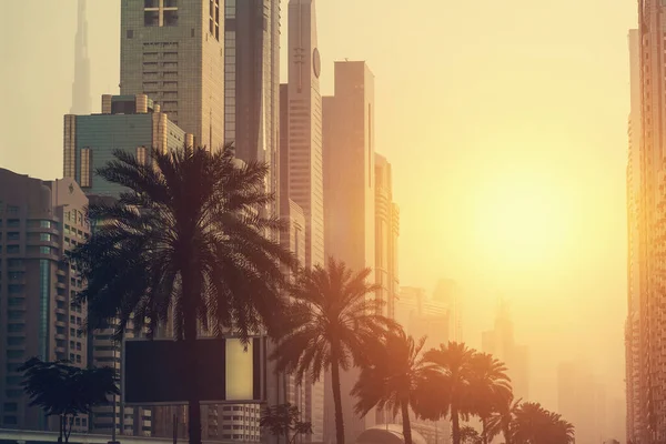 Dubai at sunset. Skyscrapers and high rise city buildings with palms in sunlight, United Arab Emirates — Stok fotoğraf